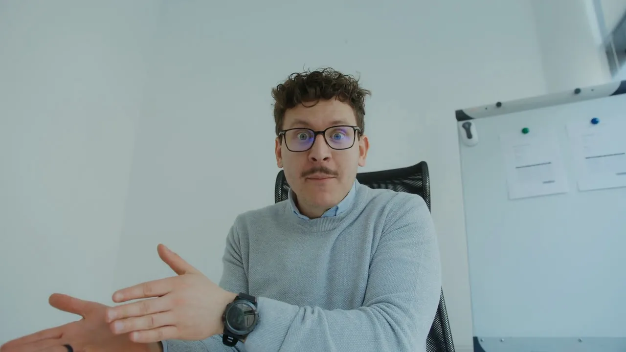 Without Backdrop Cam: a man in glasses and a blue sweater, with a whiteboard behind him